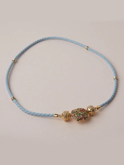 The Clara Williams Aspen Braided Light Blue Leather Mini Necklace features gold-toned beads and a multicolored stone cluster with a ClaraClasp, shown on a plain background.