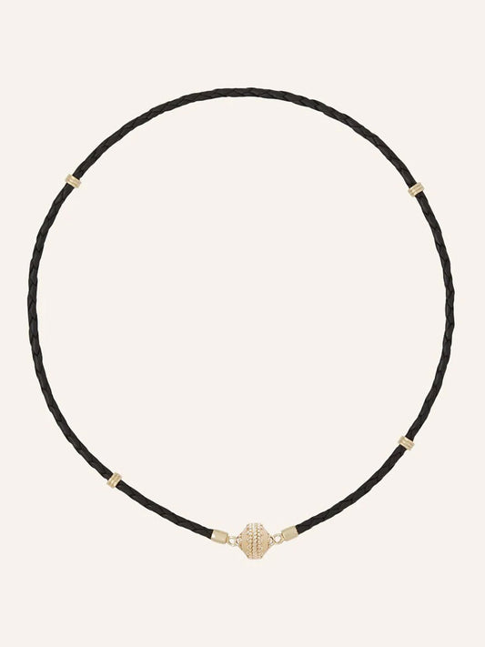 The Clara Williams Aspen Braided Leather Black Mini Necklace features a black braided leather design with gold vermeil accents and a secure sterling silver clasp, displayed on a plain light background.