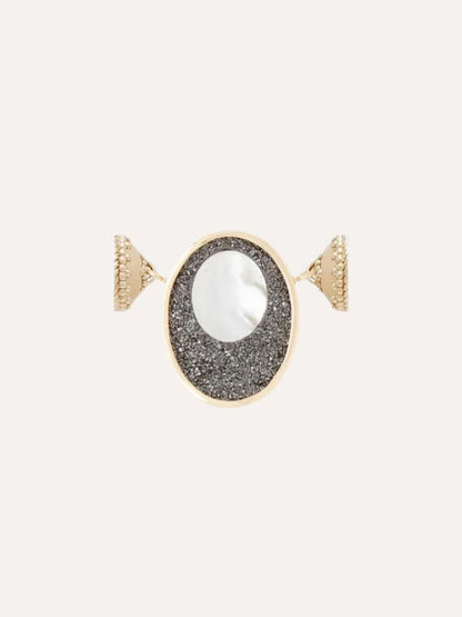 The Clara Williams 14K Black Druzy Oval Cut-Out Mini Centerpiece features an oval face with a white circular center set on a textured black druzy background, all elegantly crafted in 14K yellow gold.