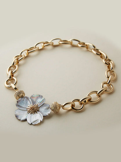 The Clara Williams Gold Coast Necklace in 14K yellow gold features oval links, a decorative flower pendant, two textured round beads, and is finished with the signature ClaraClasp.