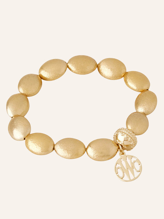 Clara Williams Gold Rush Stretch Bracelet, crafted in 14K yellow gold with a round monogrammed charm and signature textured ClaraClasp, elegantly displayed on a plain, light background.
