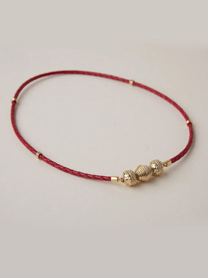The Clara Williams Gold Lantern Mini Centerpiece is a thin red braided necklace featuring 14K gold plated center beads and lantern bead accents, shown on a neutral background.