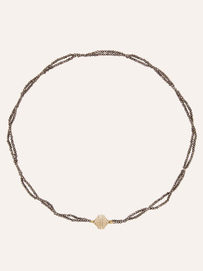 The Clara Williams Michel 2mm Coated Pyrite Double-Strand Mini Necklace features hand-strung brown chains and a central 14K yellow gold textured oval bead, elegantly displayed on a plain background.