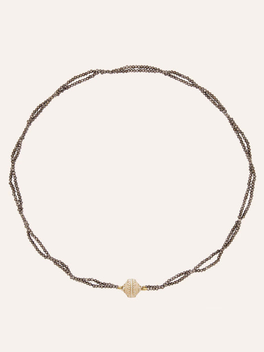 The Clara Williams Michel 2mm Coated Pyrite Double-Strand Mini Necklace features hand-strung brown chains and a central 14K yellow gold textured oval bead, elegantly displayed on a plain background.