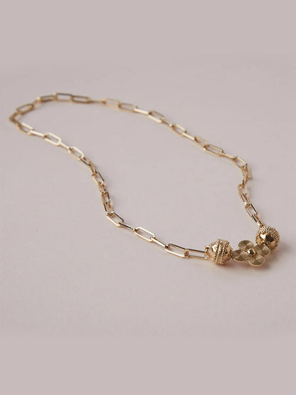 The Clara Williams Kingsbury Gold Mini Necklace features a 14K yellow gold paperclip chain with a ClaraClasp, two textured spherical beads, and a cluster of small round charms.
