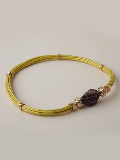 Clara Williams Small Plum Stingray Centerpiece: A yellow multi-strand necklace adorned with 14K yellow gold rings and a central bead featuring a luxurious plum-colored stingray texture, displayed on a light background.