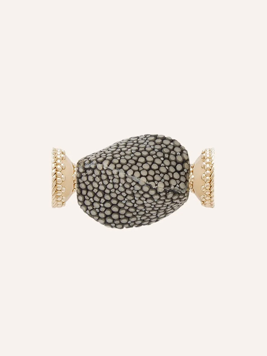 Close-up of the Clara Williams Small Charcoal Stingray Centerpiece, showcasing its textured black and white stone reminiscent of stingray hide set between two 14K yellow gold ends with decorative ridges, against a plain cream background.
