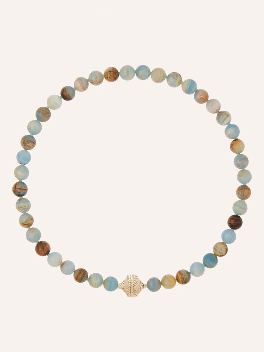 The Clara Williams Victoire 10mm Blue Calcite Necklace features round, blue and brown marbled natural calcite stones and a 14K yellow gold clasp, displayed in a circular arrangement on a plain background.