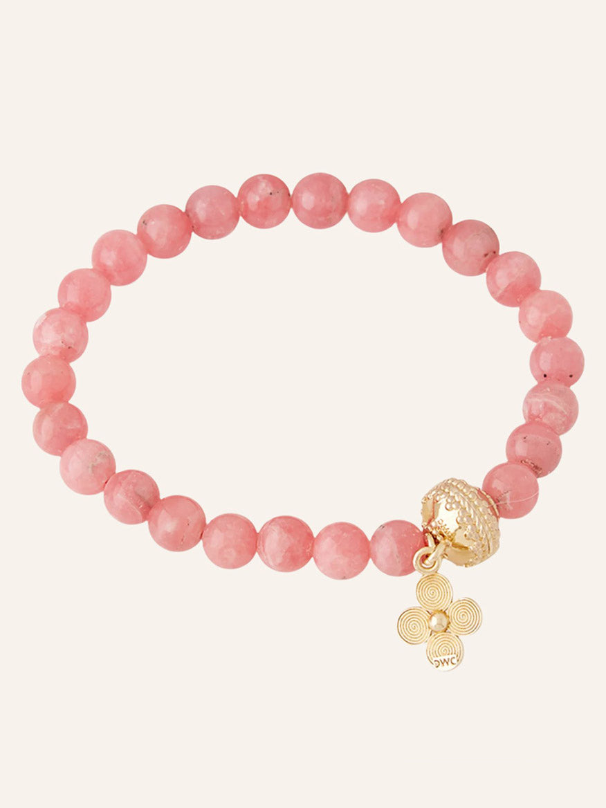 The Clara Williams Victoire 8mm Pink Rhodochrosite Stretch Bracelet features a 14K gold bead, a gold charm adorned with three spiral designs, and a textured gold bead accent. This limited edition piece adds an elegant touch to any ensemble and is beautifully displayed against a plain background.