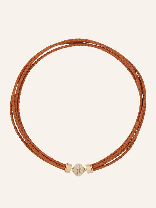 The Clara Williams Wellington Braided Leather Saddle Necklace features a double-wrap design in Saddle Brown braided leather with a 14K yellow gold cylindrical clasp, shown against a plain light background.
