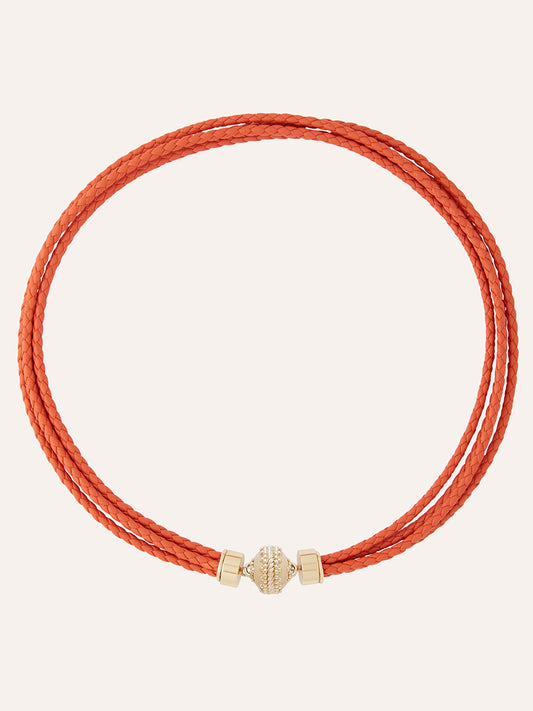 Clara Williams Wellington Braided Leather Orange Necklace featuring a double-wrap orange braided leather design, a 14K yellow gold magnetic clasp, and a decorative central bead, displayed on a plain background.