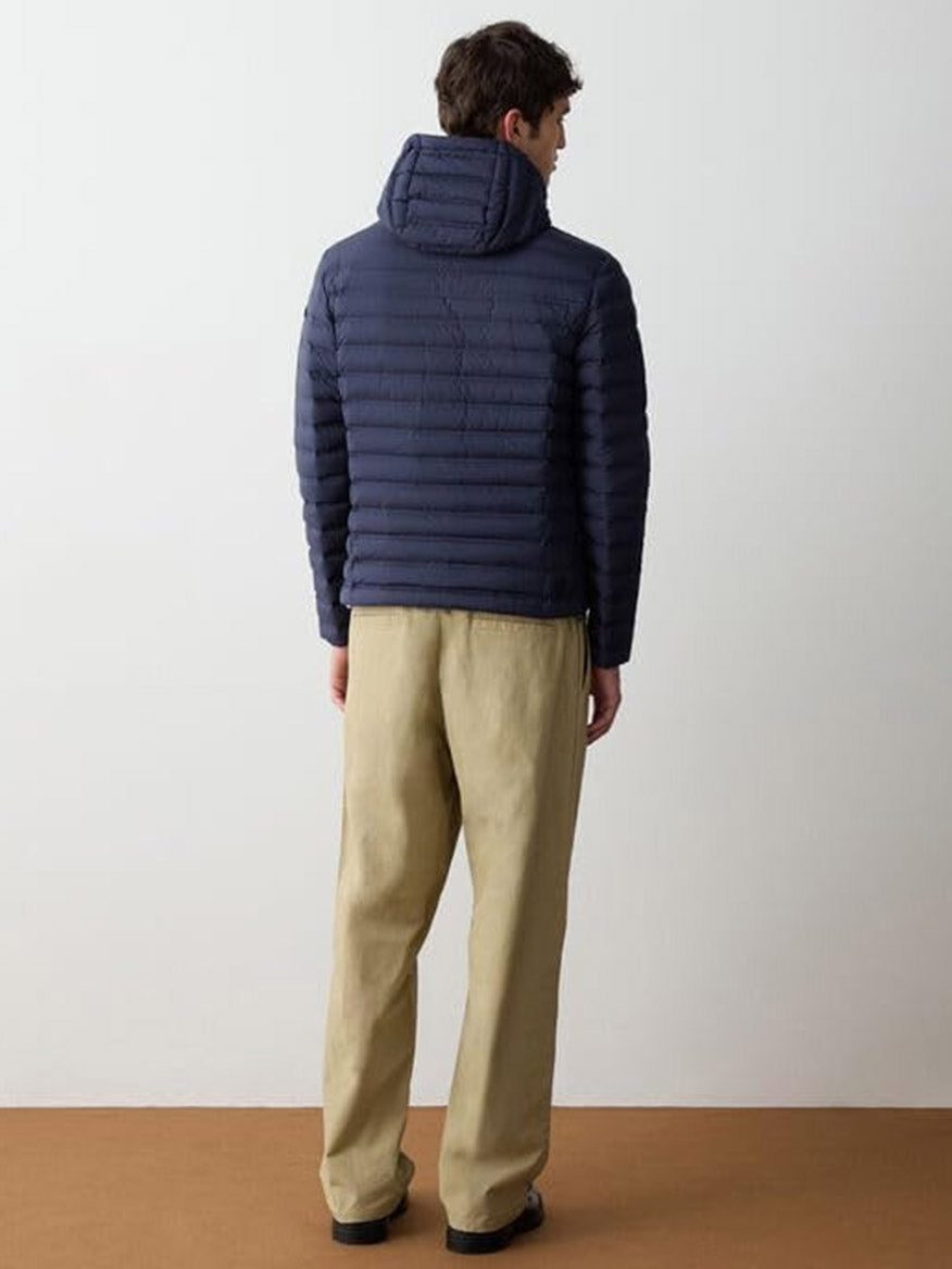 A person stands facing away, wearing the Colmar Underscore Down Hooded Zip Jacket in Navy Blue/Vulcan with loose beige pants, set against a plain light background.