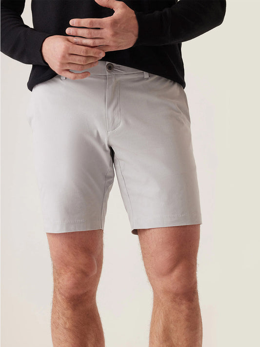 A person wearing a black long-sleeve shirt and DEKE Galaxy Bermuda Ultra 4X Stretch Twill shorts in Stone, standing with hands near the waist.