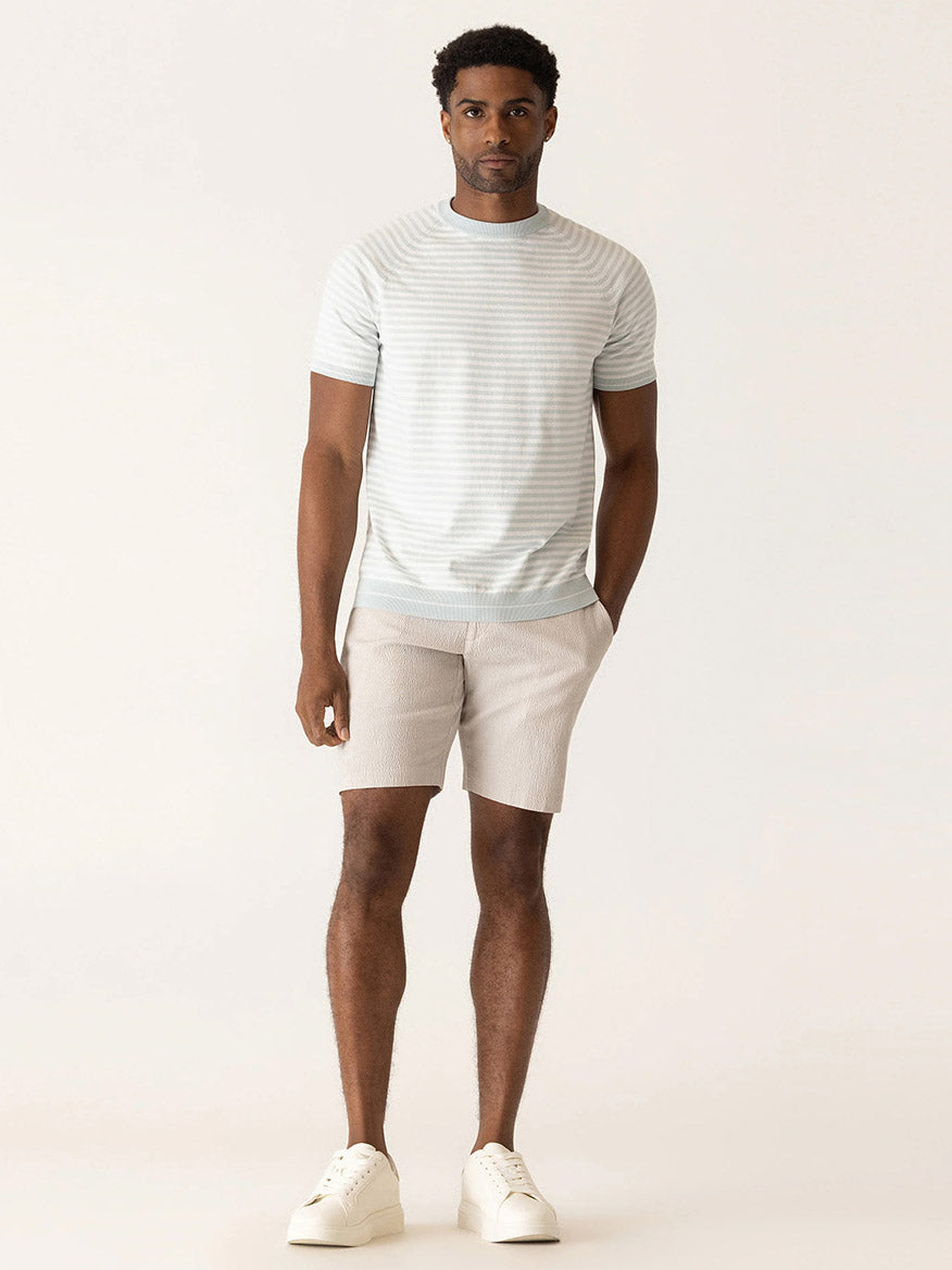 A man faces forward in a light striped Supernatural Seersucker t-shirt, DEKE Galaxy Bermuda Supernatural Seersucker in Sand, and white sneakers against a plain background—effortless summer style.