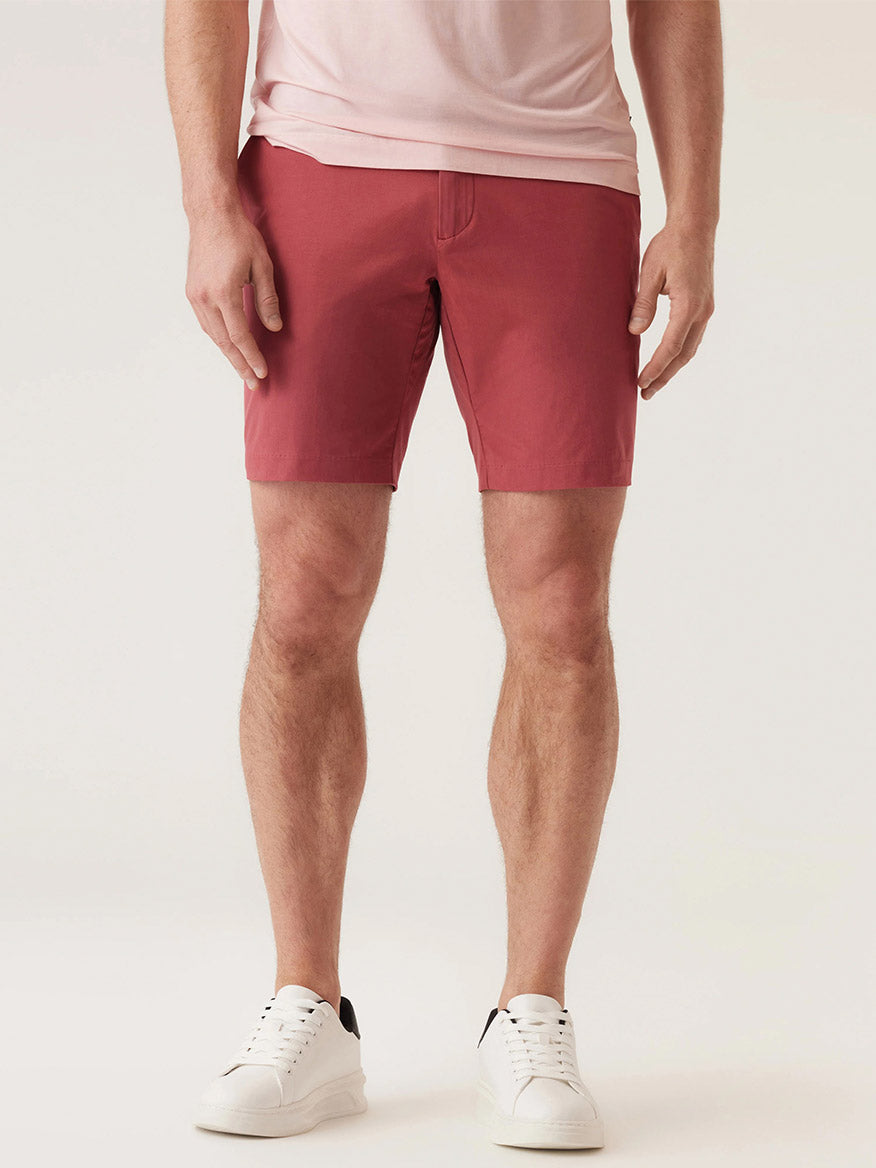 A person wearing a light pink T-shirt, white sneakers, and DEKE Galaxy Bermuda Ultra 4X Stretch Twill in Nantucket Red stands facing forward against a plain background.