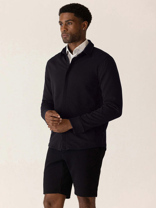 A man wearing a black DEKE Getaway Shirt Jacket in Black Twilight Twill Jersey™ over a white collared shirt, paired with black shorts.