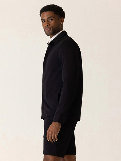 A man wearing a black DEKE Getaway Shirt Jacket in Black Twilight Twill Jersey™ over a white collared shirt.