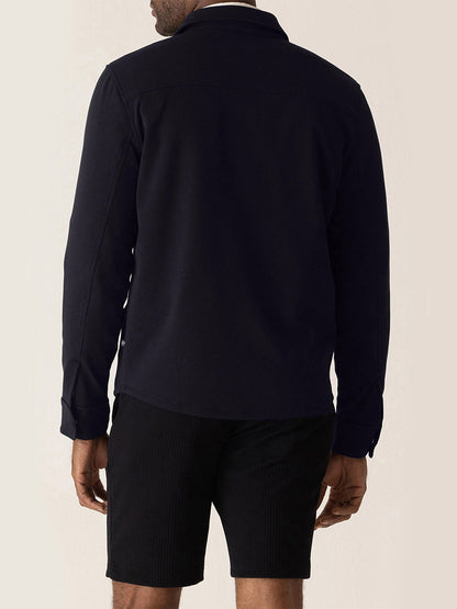 Back view of a person wearing a navy DEKE Getaway Shirt Jacket in Midnight Twilight Twill Jersey™ and black shorts.