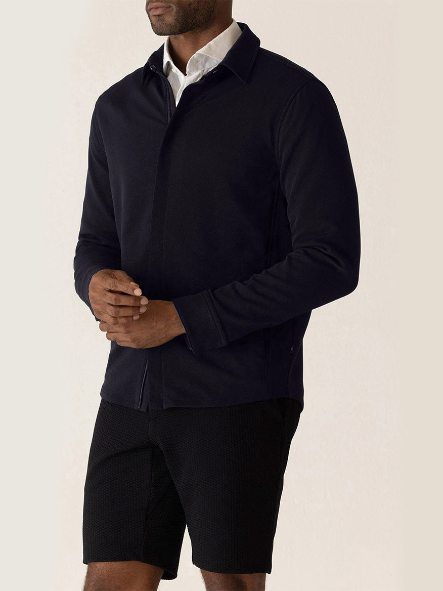 A man wearing a DEKE Getaway Shirt Jacket in Midnight Twilight Twill Jersey™ over a white collared shirt, paired with black shorts.