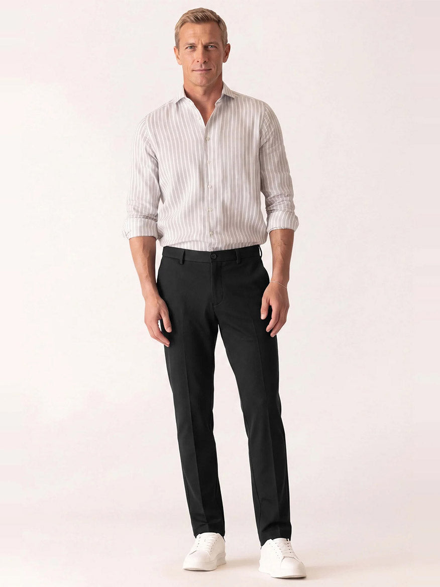 Man wearing a lightweight knit vertical striped button-down shirt, DEKE Mobile Flat Front Pant in Black Twilight Twill Jersey™, and white sneakers.
