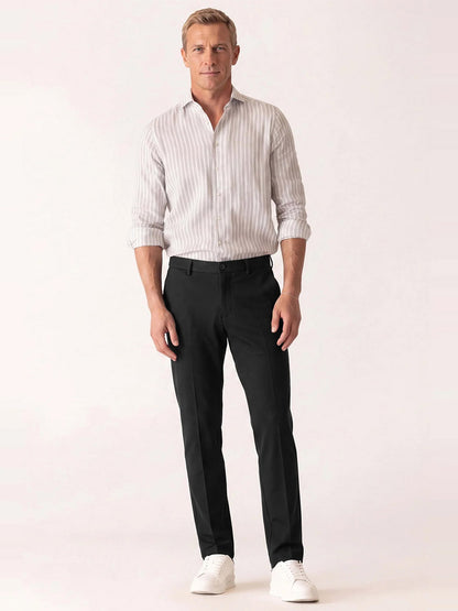 Man wearing a lightweight knit vertical striped button-down shirt, DEKE Mobile Flat Front Pant in Black Twilight Twill Jersey™, and white sneakers.