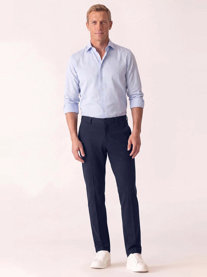 A man wearing a light blue button-down shirt, DEKE Mobile Flat Front Pant in Midnight Twilight Twill Jersey™, and white sneakers.