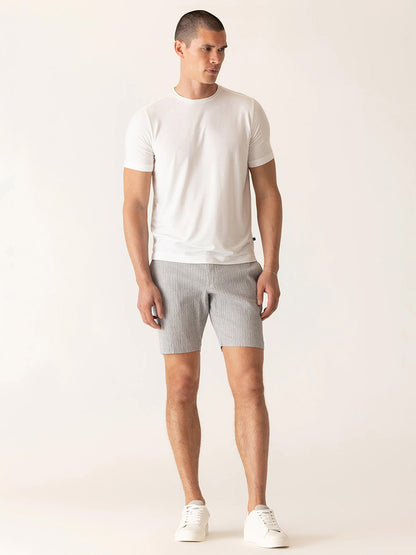 A man stands in a neutral pose wearing a white t-shirt, white sneakers, and DEKE Oasis Bermuda Supernatural Seersucker shorts in Grey/Natural against a plain light background.