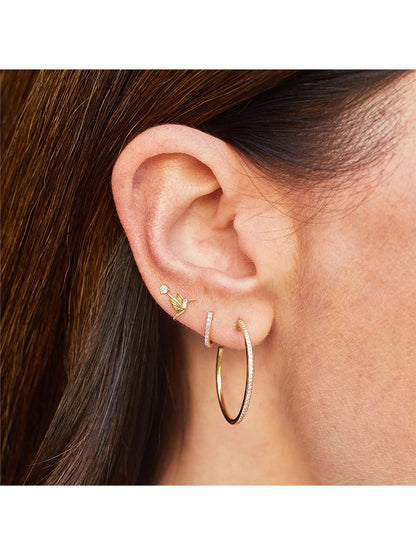 Close-up of an ear with three piercings, featuring an EF Collection Mini Hummingbird Stud Earring in Yellow Gold, a star-shaped earring, and a large hoop earring with butterfly backings.