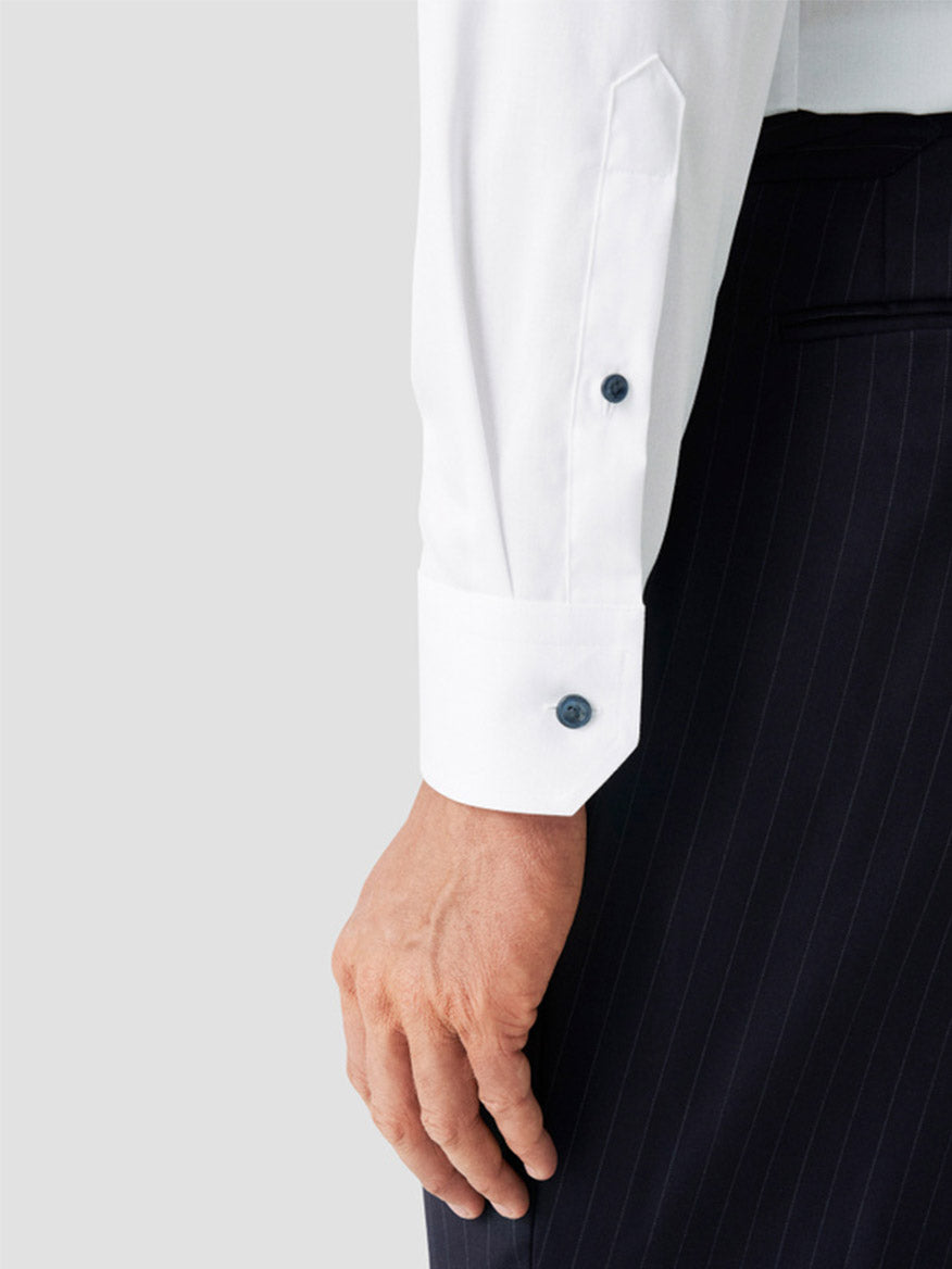 A close-up of a person’s arm wearing the Eton Classic Fit Solid Signature Twill Dress Shirt in White with Navy Details, paired with dark pinstriped trousers.