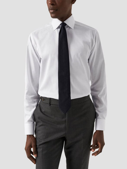 A person stands against a plain light background wearing the Eton Classic Fit Twill Dress Shirt in White, wrinkle-free, paired with a black tie and gray trousers.