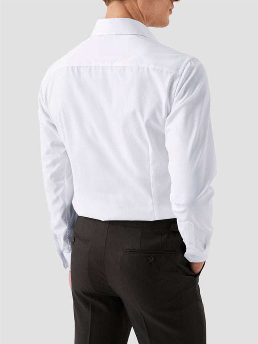 A man is seen from behind wearing the Eton Contemporary Fit White Extreme Cut Away Dress Shirt and black dress pants against a plain light gray background.