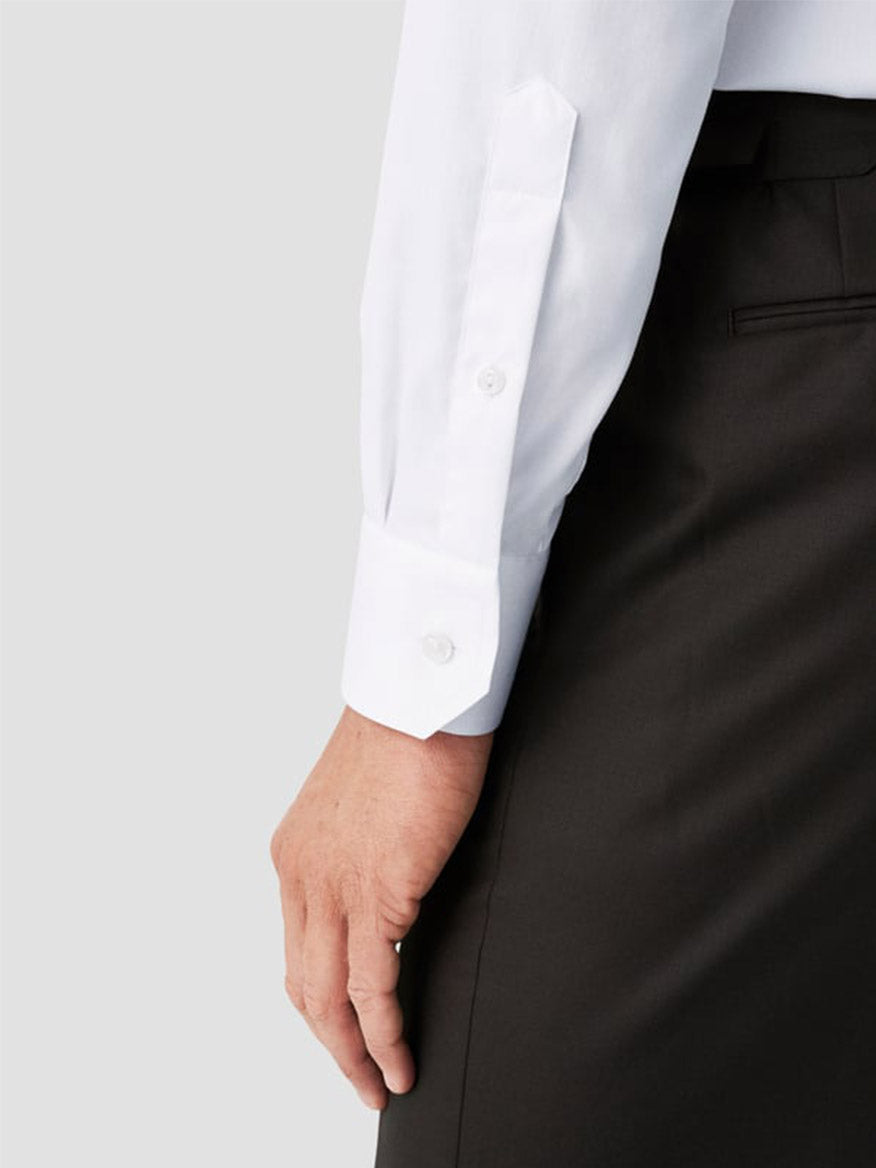 A person wearing an Eton Contemporary Fit White Extreme Cut Away Dress Shirt and black pants, shown from the waist down, with their left arm hanging by their side.