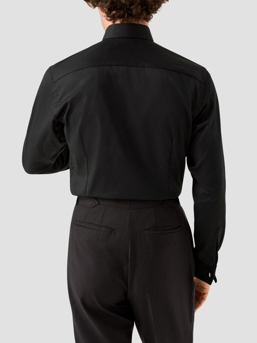 A person wearing the Eton Slim Fit Fine Striped Bib Evening Shirt in Black - French Cuff and black trousers, shown from the back against a plain light gray background.