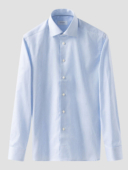 The Eton Contemporary Fit Fine Striped Signature Twill Dress Shirt in light blue features long sleeves, a spread collar, white buttons, and a subtle stripe pattern—perfect for business style. Shown on a plain gray background.
