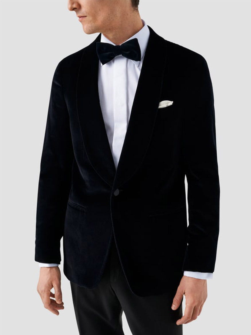 A man wearing a black velvet tuxedo jacket, Eton Slim Fit Fly Front Evening Dobby Shirt in White, black bow tie, and white pocket square stands against a plain light gray background.