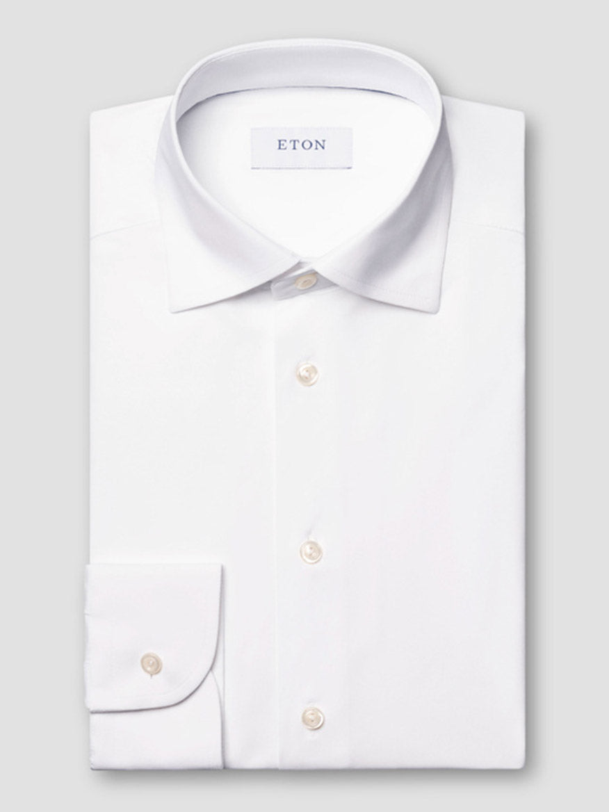 The Eton Slim Fit White Four-Way Stretch Shirt with a classic collar and white buttons is neatly folded and displayed on a plain light grey background.