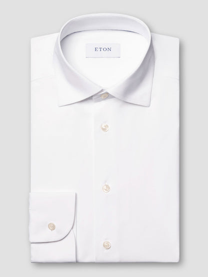 The Eton Slim Fit White Four-Way Stretch Shirt with a classic collar and white buttons is neatly folded and displayed on a plain light grey background.