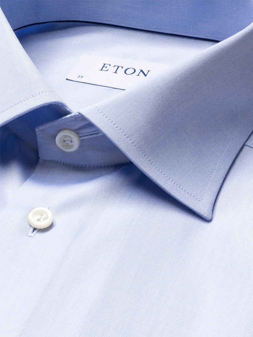 Close-up of the Eton Contemporary Fit Solid Signature Twill Dress Shirt in light blue, featuring French cuffs, a spread collar, white buttons, and part of the brand label inside the collar.