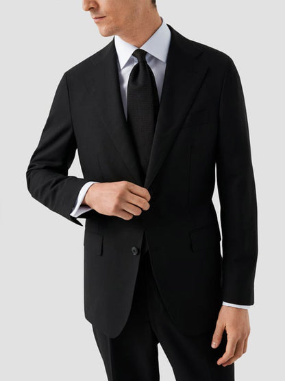 A man in a black suit and tie adjusts his jacket, wearing the Eton Slim Fit Solid Signature Twill Dress Shirt in White with French cuffs, standing against a plain light gray background.
