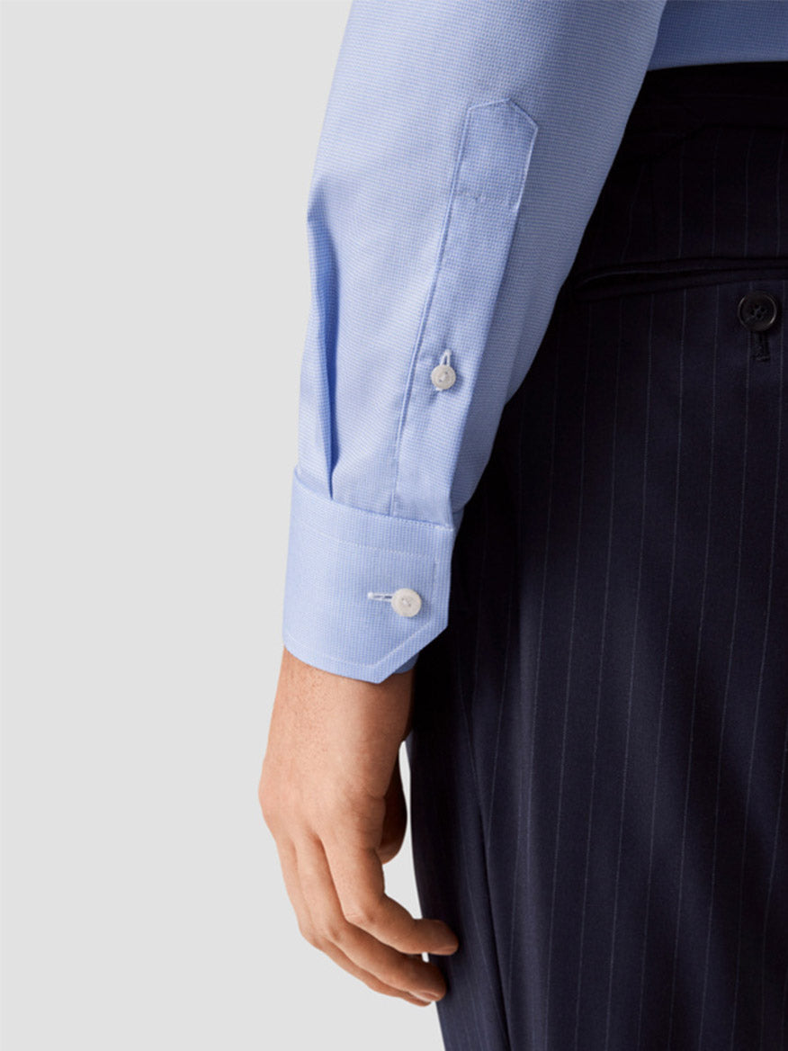 A person is wearing an Eton Contemporary Fit Light Blue Houndstooth Dress Shirt with buttoned cuffs and dark pinstripe trousers; only the arm and part of the torso are visible.