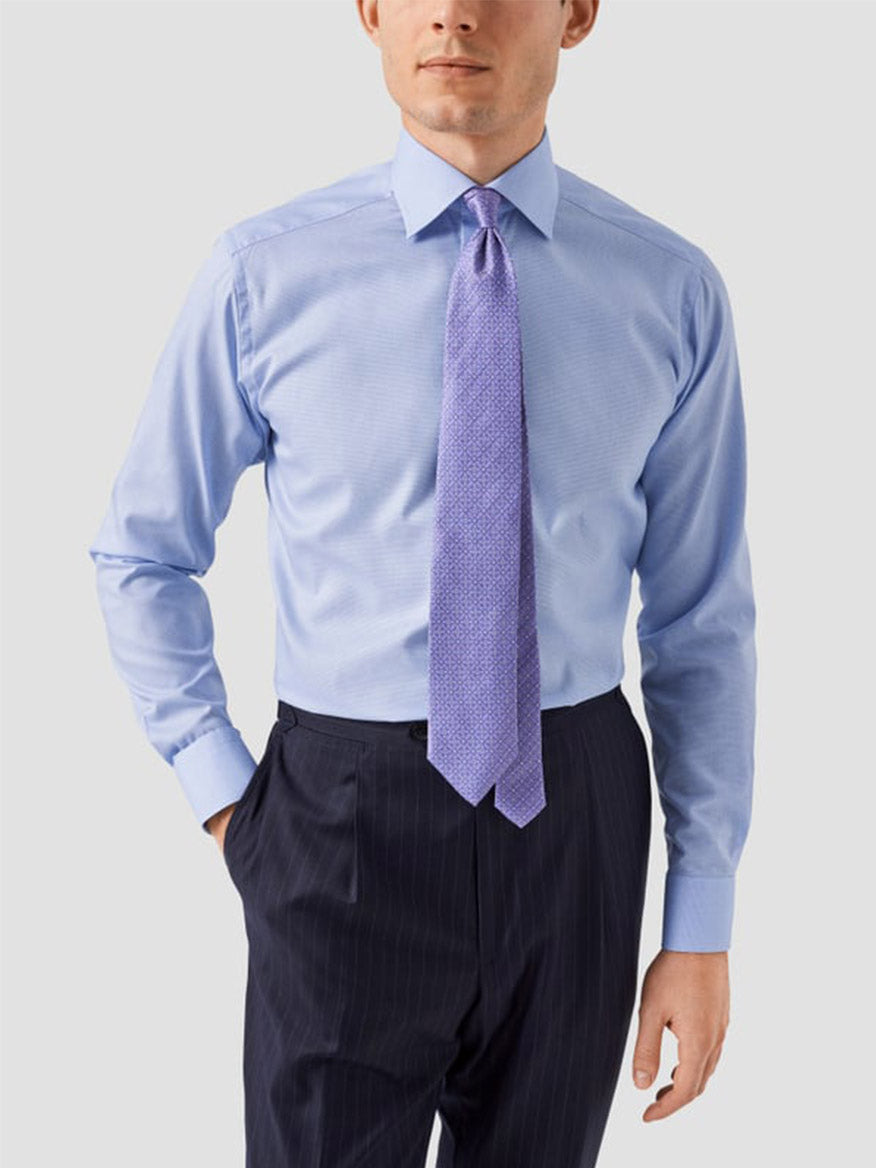 Man wearing an Eton Contemporary Fit Light Blue Houndstooth Dress Shirt, paired with dark pinstripe pants and a wide light purple patterned tie, standing against a plain light background, showcasing a modern style.