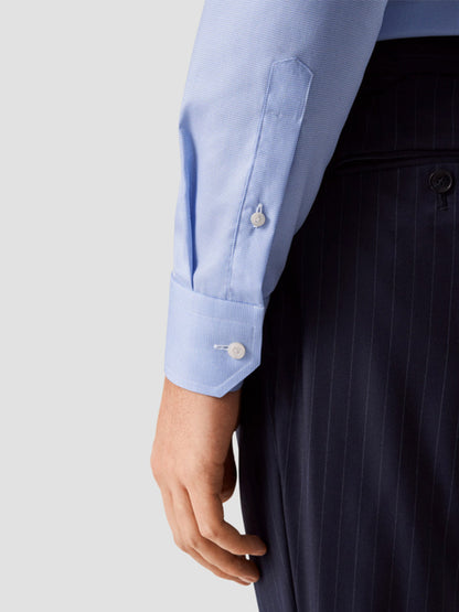 A person wears the Eton Slim Fit Houndstooth Fine Twill Dress Shirt in Light Blue, shown from the waist down with relaxed arm, paired with dark pinstripe trousers.