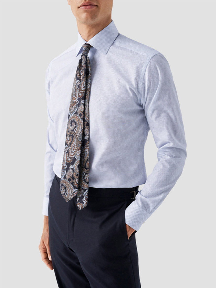 A man wears an Eton Contemporary Fit Sky Blue Micro Print Dress Shirt, a dark paisley tie, and dark trousers, standing with one hand in his pocket against a plain background.