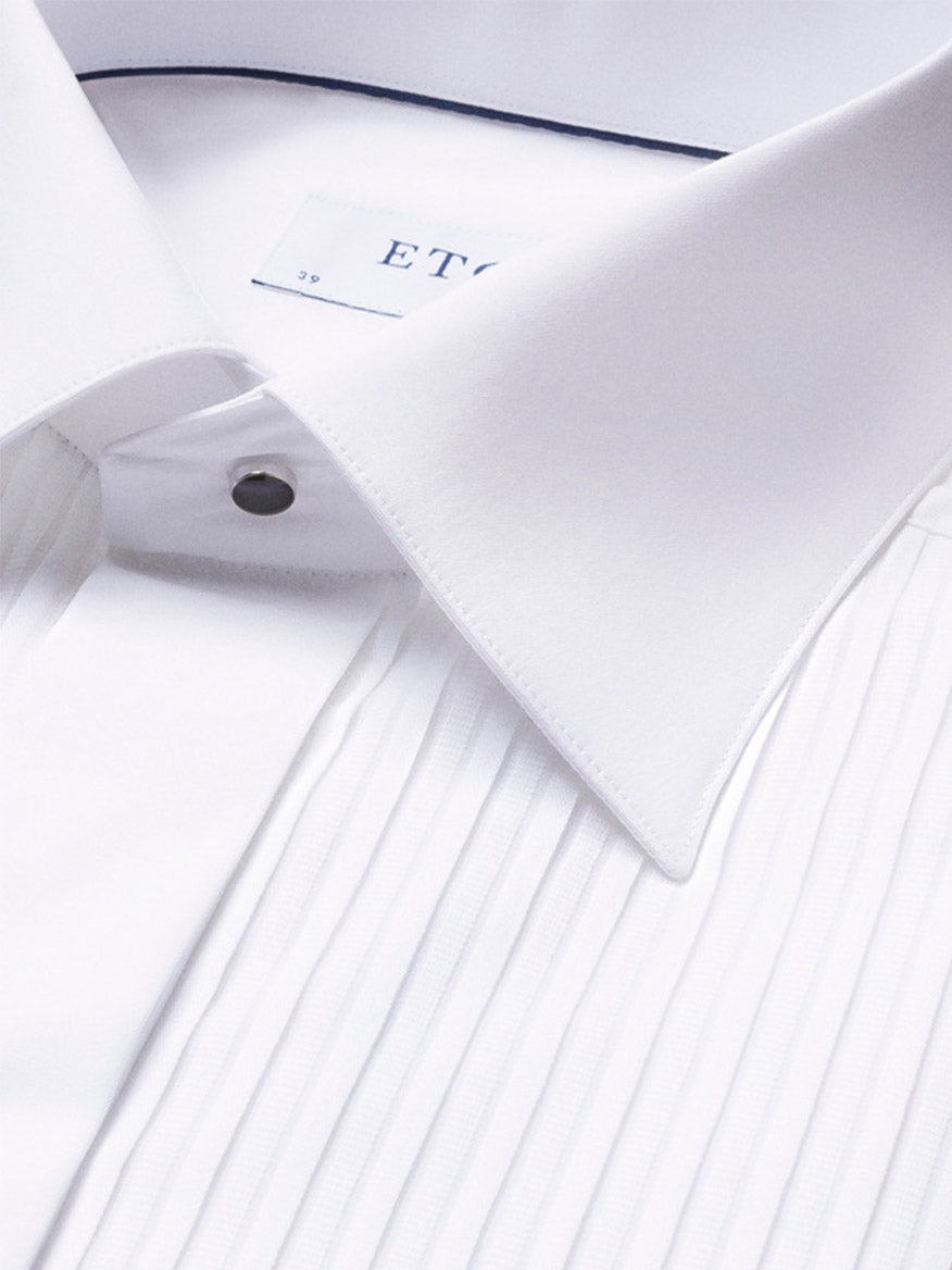 Close-up of the Eton Contemporary Fit Plissé Black Tie Dress Shirt, featuring a white pleated front, pointed collar, and metal stud button; part of the clothing label is visible inside the collar.