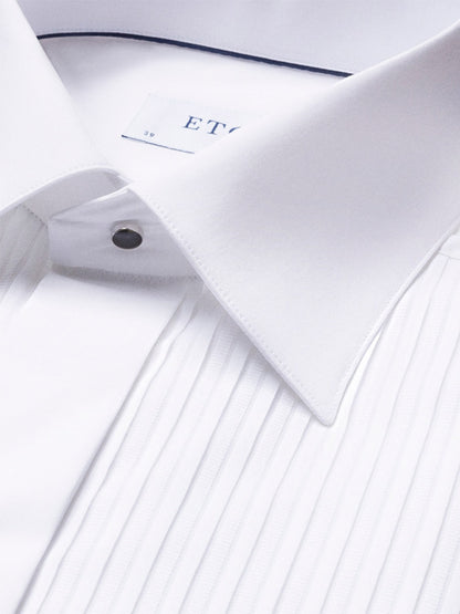 Close-up of the Eton Contemporary Fit Plissé Black Tie Dress Shirt, featuring a white pleated front, pointed collar, and metal stud button; part of the clothing label is visible inside the collar.