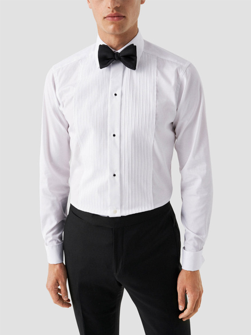 A man wears the Eton Contemporary Fit Plissé Black Tie Dress Shirt with a black bow tie and black dress pants, standing against a plain light gray background.
