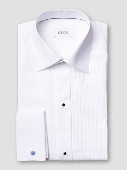 The Eton Slim Fit Plissé Bib-Front Tuxedo Shirt in White features a pleated front, French cuffs, and black stud buttons—an elegant choice for black-tie events, shown neatly folded on a light gray background.