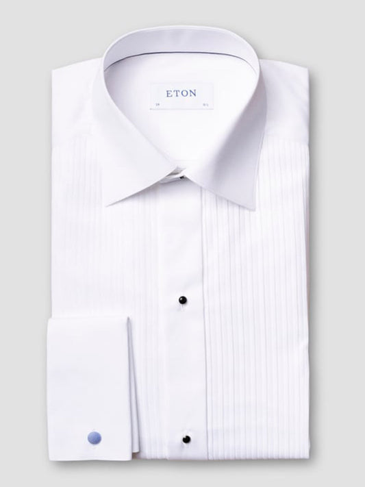 The Eton Slim Fit Plissé Bib-Front Tuxedo Shirt in White features a pleated front, French cuffs, and black stud buttons—an elegant choice for black-tie events, shown neatly folded on a light gray background.