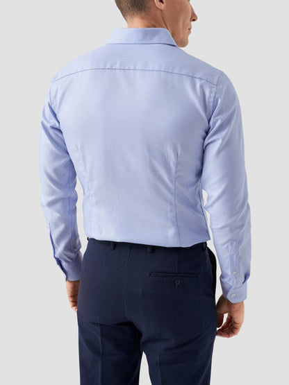 A man wearing the Eton Contemporary Fit Semi Solid Dobby Dress Shirt in Light Blue and dark navy trousers, viewed from the back against a plain light gray background.