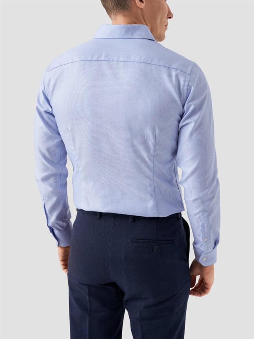 A man seen from behind wears the Eton Slim Fit Semi Solid Dobby Dress Shirt in Light Blue with dark blue dress pants, set against a plain light background.